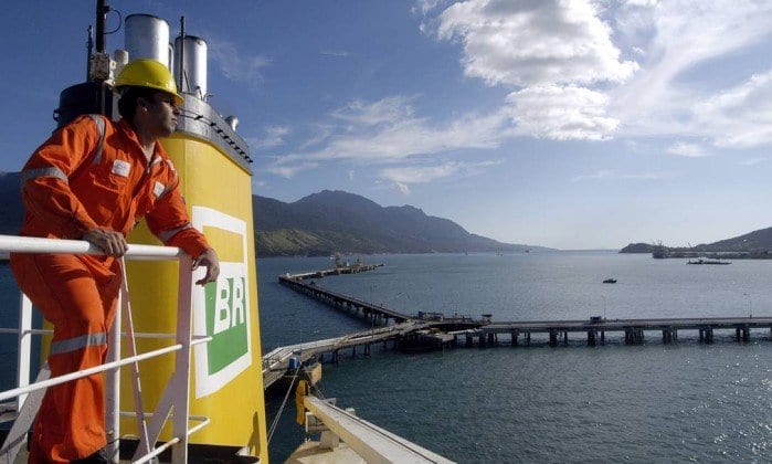 Navio-cisterna da Petrobras com trabalhador uniformizado, com macacão laranja com a logomarca BR e capacete de proteção amarelo, encostado em parapeito no andar mais alto da embarcação (Foto: Divulgação Transpetro)