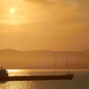 Preço do petróleo em alta enquanto investidores assimilam dados de relatório da Opep. Na imagem: Navio tanque transporta petróleo com céu em tons de amarelo com pôr do sol, e montanha, ao fundo (Foto Creative Commons)