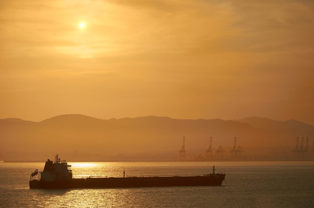 Preço do petróleo em alta enquanto investidores assimilam dados de relatório da Opep. Na imagem: Navio tanque transporta petróleo com céu em tons de amarelo com pôr do sol, e montanha, ao fundo (Foto Creative Commons)