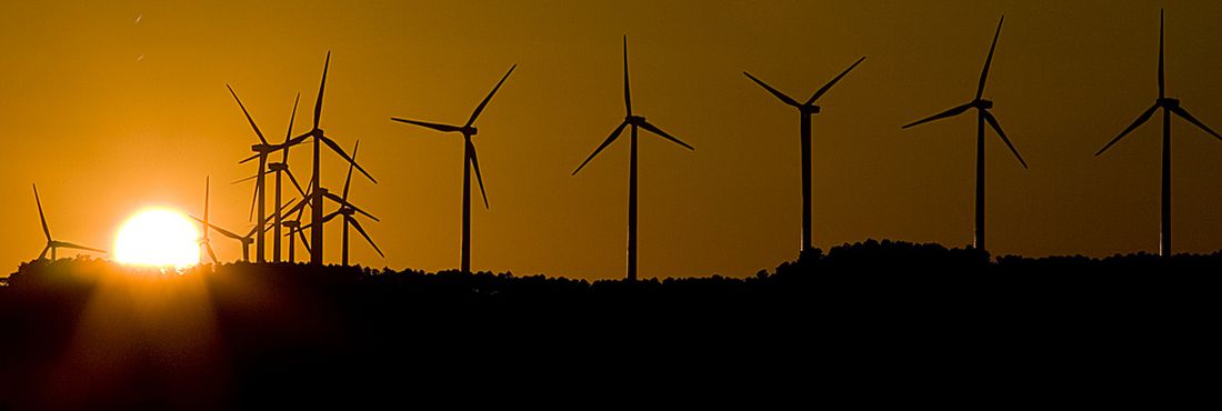 Parque eólico ao anoitecer. Na imagem aparecem três aerogeradores