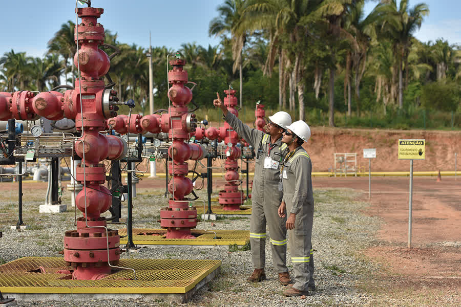 Na imagem: Dois trabalhadores (homens, uniformizados e com óculos e capacetes) realizam inspeção em rede de dutos, na cor vermelha, em operação terrestre da Eneva na Bacia do Parnaíba, no Maranhão (Foto: Divulgação)