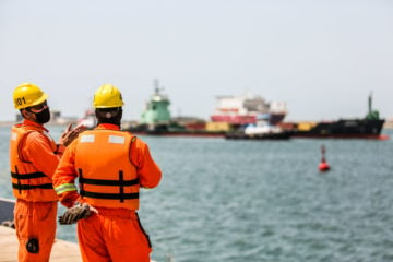 Porto do Açu licencia 2 GW de eólica offshore no Rio de Janeiro. Na imagem: Trabalhadores, uniformizados, conversando no cais do Porto do Açu, e olhando para embarcações no mar (Foto: Divulgação/Porto do Açu)