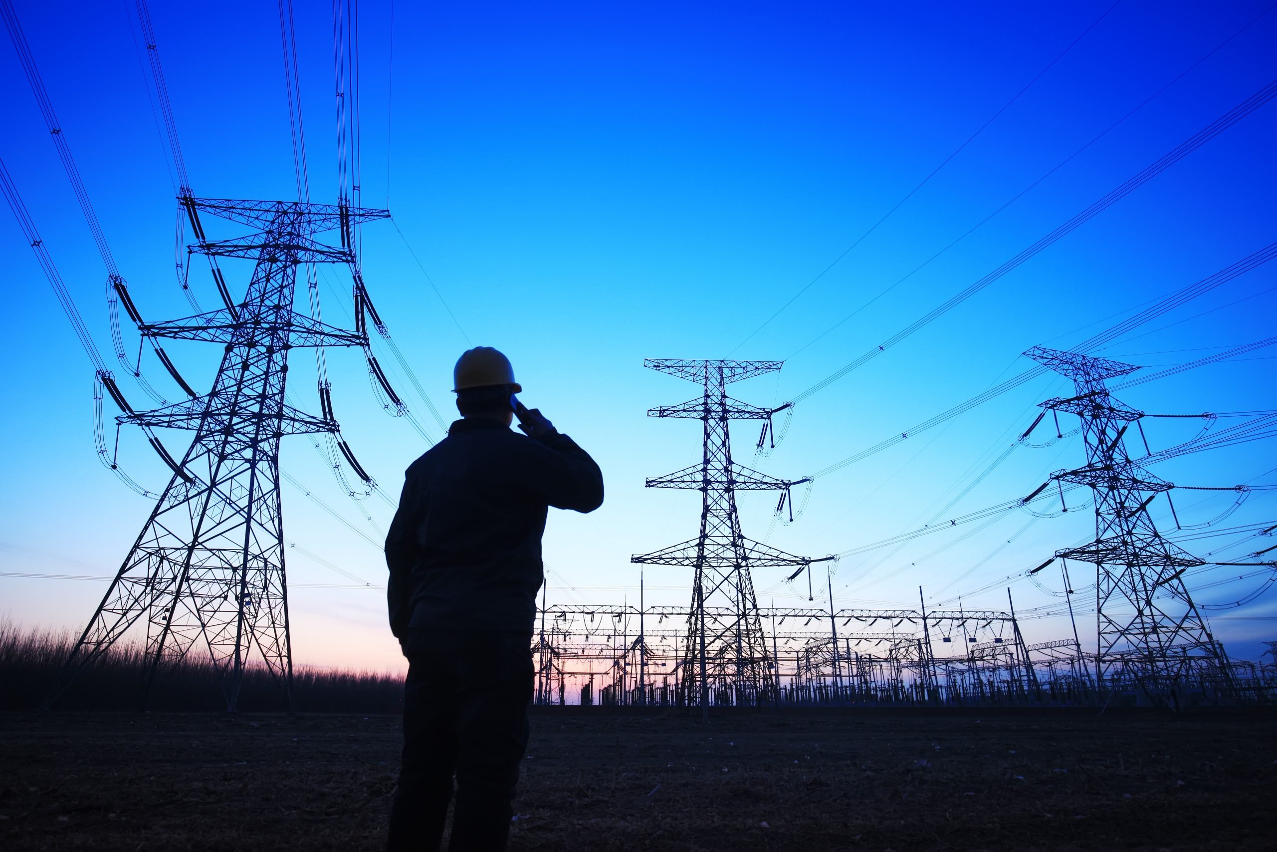 Aneel homologa resultado do Leilão de Energia Nova A-5 de setembro de 2021. Na imagem: Foto à contraluz de operador do setor elétrico ao telefone e, ao fundo, linhas de transmissão, com céu azul