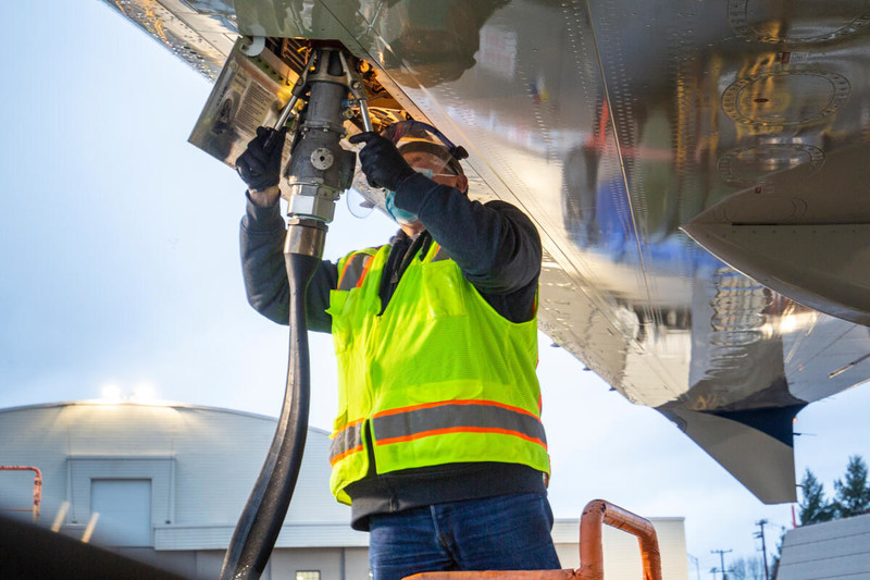 Produzido a partir de resíduos agrícolas, o SAF será misturado no percentual de 30% ao combustível fóssil usado pela Boeing. Na imagem: Técnico de manutenção de aviação, com colete de segurança amarelo fosforescente, carrega combustível de aviação sustentável no Boeing ecoDemonstrator 2021, com mangueira conectada verticalmente na parte de baixo da aeronave (Foto: Divulgação Boeing)