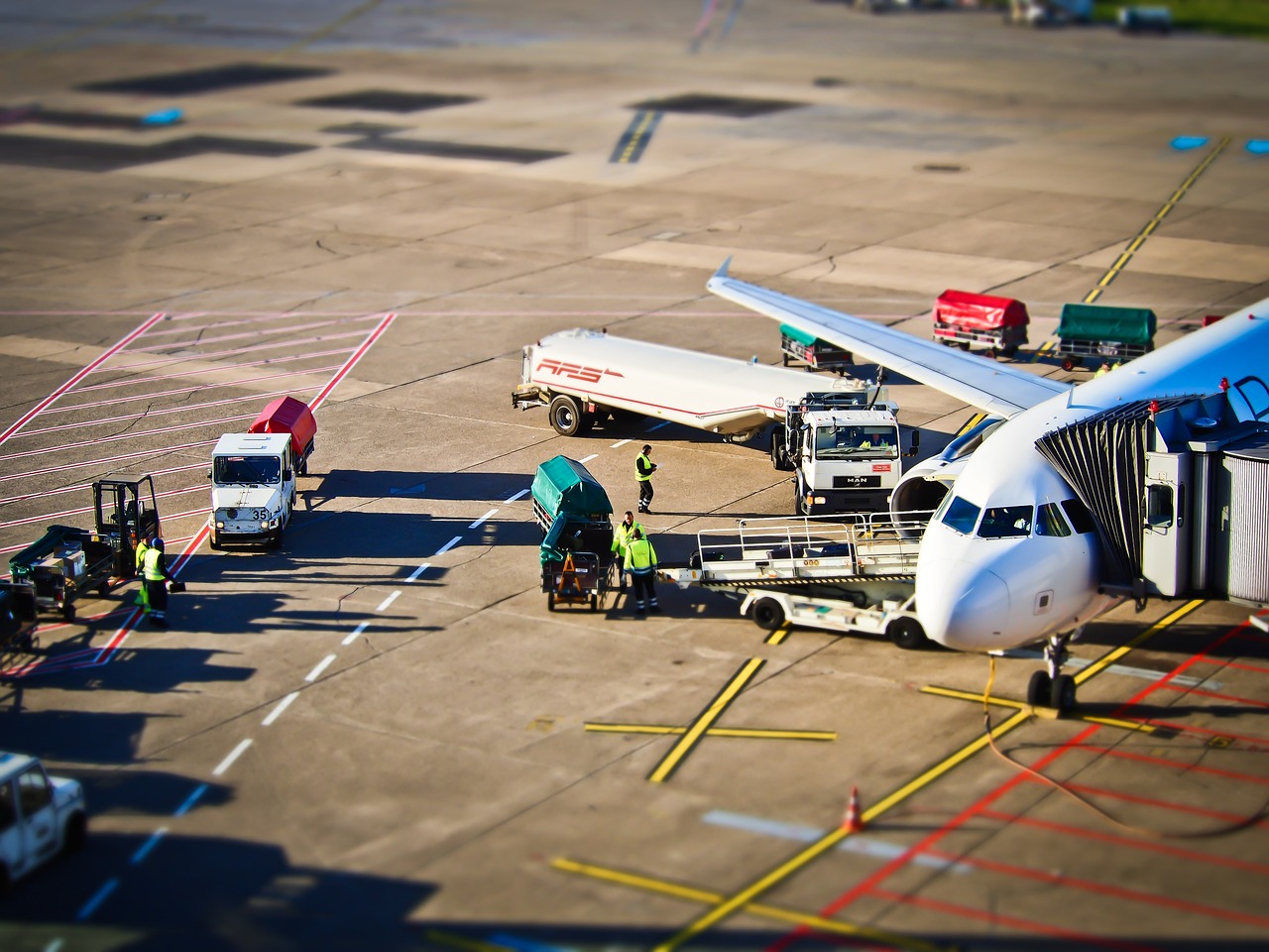 Foto aérea de avião sendo abastecido em aeroporto, com caminhões-tanque e trabalhadores próximos à aeronave