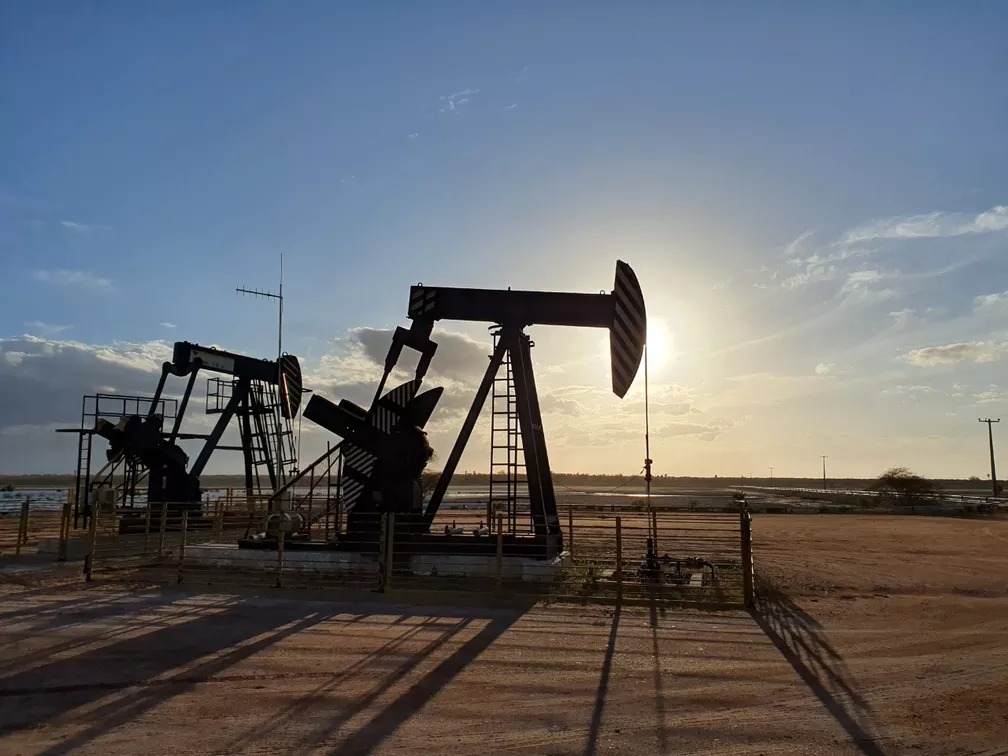 Na imagem: Foto à contraluz de cavalos-de-pau para exploração de petróleo em campo terrestre do Polo Potiguar, com pôr-do-sol ao fundo; conjunto de ativos inclui toda infraestrutura associada de processamento, refino, logística, armazenamento, transporte e escoamento de óleo e gás (Foto: Divulgação 3R Petroleum)