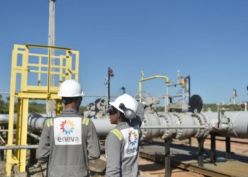 Leilão de térmicas da Eletrobras contrata três usinas no Norte e dá vazio no Nordeste. Na imagem: Planta da Eneva com dois trabalhadores negros (um homem e uma mulher), fotografados de costas conversando, com uniformes cinzas e capacetes de proteção brancos (Foto: Divulgação)