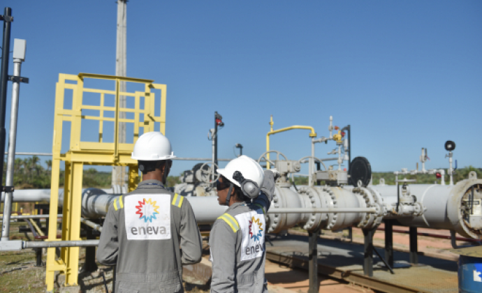 Leilão de térmicas da Eletrobras contrata três usinas no Norte e dá vazio no Nordeste. Na imagem: Planta da Eneva com dois trabalhadores negros (um homem e uma mulher), fotografados de costas conversando, com uniformes cinzas e capacetes de proteção brancos (Foto: Divulgação)