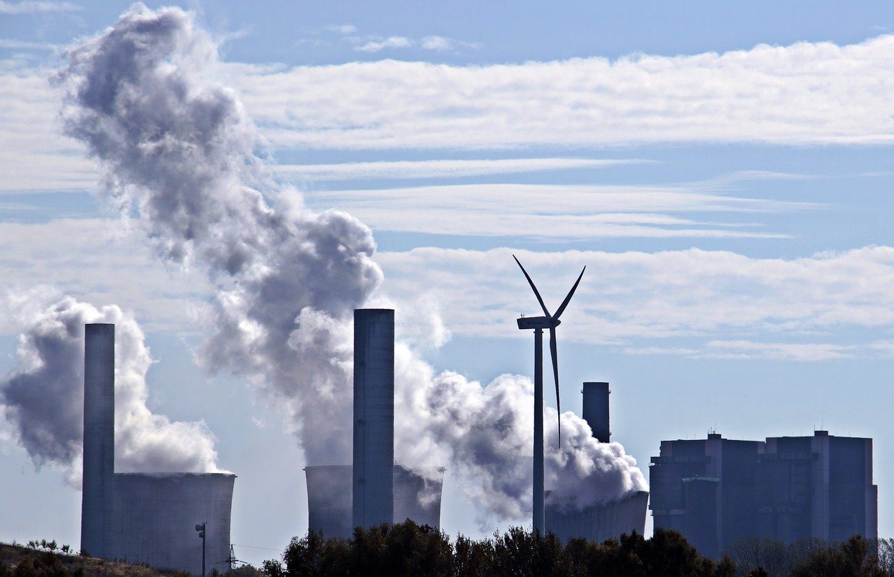 A peregrinação das termelétricas. Na imagem: Turbina eólica e, ao fundo, usina térmica movida a carvão mineral emitindo grande volume de emissões poluentes (Foto: S. Hermann/F. Richter/Pixabay)