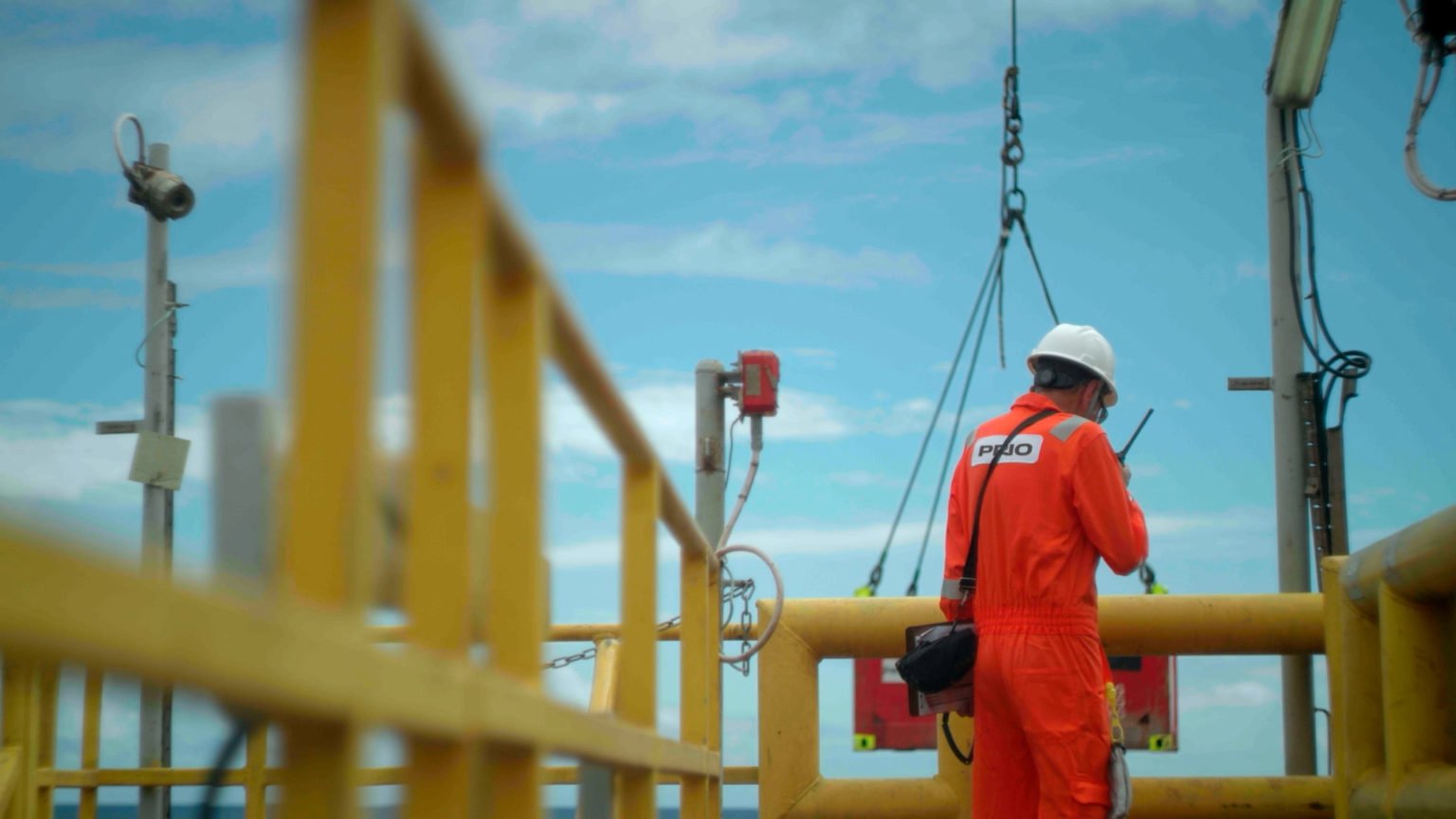 Independentes vão investir US$ 10 bilhões em projetos vendidos pela Petrobras. Na imagem: Funcionário da PRIO de uniforme laranja e capacete branco, de costas, em plataforma na Bacia de Campos (Foto: Cortesia)