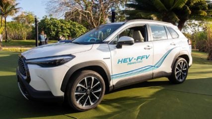 Transição econômica: substituição de SUVs tradicionais por híbridos. Na imagem: SUV híbrido flex branco da Toyota; na porta do lado do motorista está escrito, em verde: HEV-FFV – híbrido flex (Foto: Reprodução VRUM)