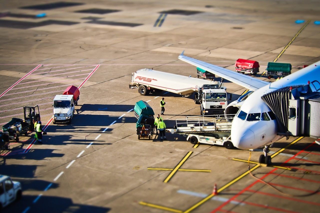 Foto aérea de avião sendo abastecido em aeroporto, com caminhões-tanque e trabalhadores próximos à aeronave