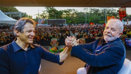 Fernando Haddad [à esquerda] e Rui Costa confirmados no governo Lula [à direita]; Haddad e Lula, em primeiro plano, e, ao fundo, grande número de pessoas sentadas numa arquibancada (Foto: Ricardo Stuckert/PT)