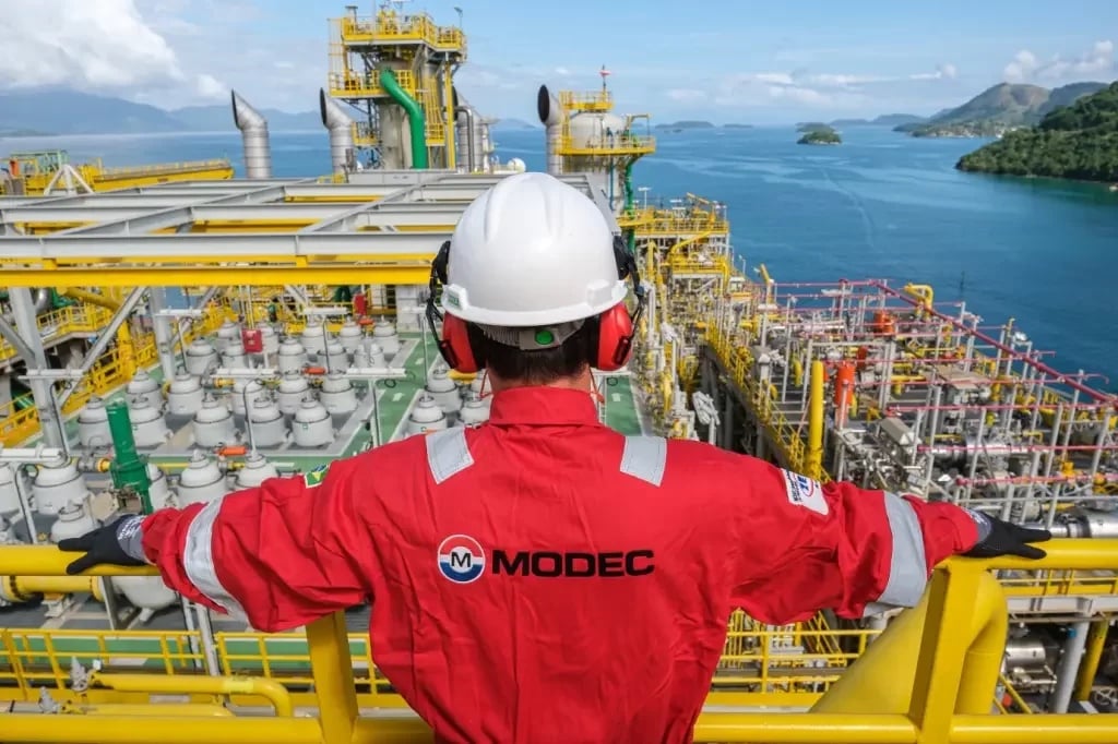 Vagas em petróleo e gás: Modec abre 267 postos de trabalho onshore e offshore no RJ e SP. Na imagem: Trabalhador com capacete branco e uniforme laranja da Modec observa plataforma (Foto: Divulgação)