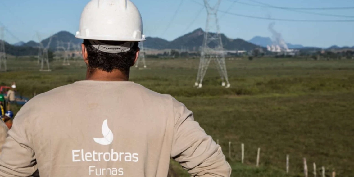 Na imagem: Funcionário de Furnas, subsidiária da Eletrobras, em frente a torres de transmissão de energia elétrica, de costas e com uniforme e capacete (Foto: Divulgação)