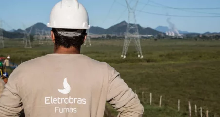 Na imagem: Funcionário de Furnas, subsidiária da Eletrobras, em frente a torres de transmissão de energia elétrica, de costas e com uniforme e capacete (Foto: Divulgação)