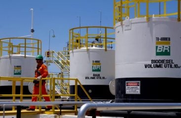 Nova especificação do biodiesel: grande passo, inclusive cultural. Na imagem: Trabalhadores de uniforme laranja passam em frente a tanques de armazenamento de combustíveis em planta da PBIO – Petrobras Biocombustível (Foto: Divulgação PBIO)