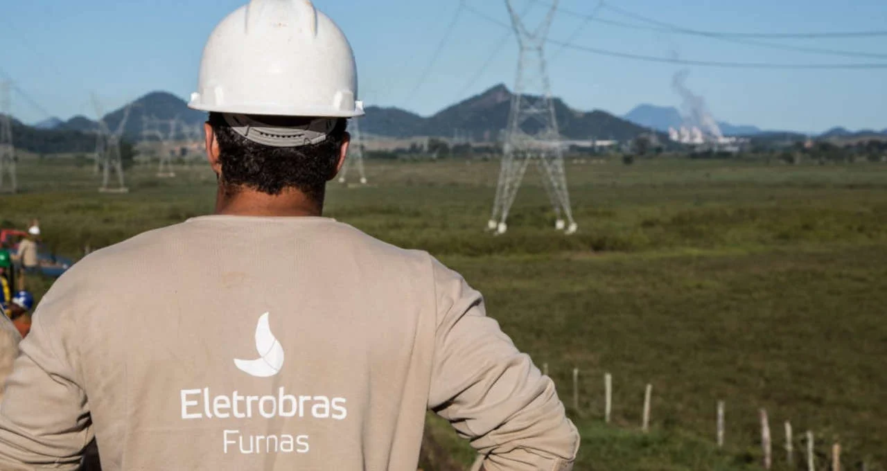 Eletrobras abre mais 369 vagas de emprego para ensino técnico e superior. Na imagem: Funcionário de Furnas, subsidiária da Eletrobras, em frente a torres de transmissão de energia elétrica, de costas e com uniforme e capacete (Foto: Divulgação)