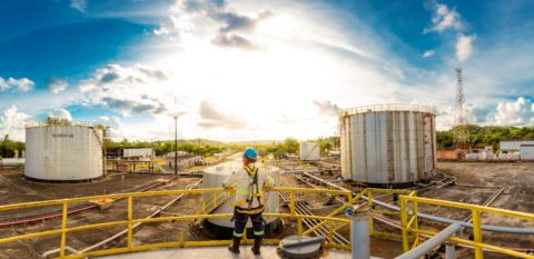 PetroReconcavo assina contrato de fornecimento de gás natural com Copergás, em Pernambuco. Na imagem: Operação da PetroRecôncavo no Polo Miranga, na Bahia; Trabalhador, com equipamentos de segurança, observa a planta, do alto, e encostado em parapeito amarelo (Foto: Cortesia PetroRecôncavo)