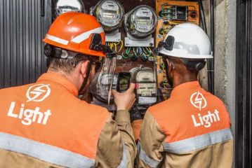 Light apresenta plano para pagar dívidas; veja a íntegra. Na imagem: Técnicos da Light, um homem branco e um negro uniformizados, realizam medições e fotografam relógio de energia (Foto: Divulgação)