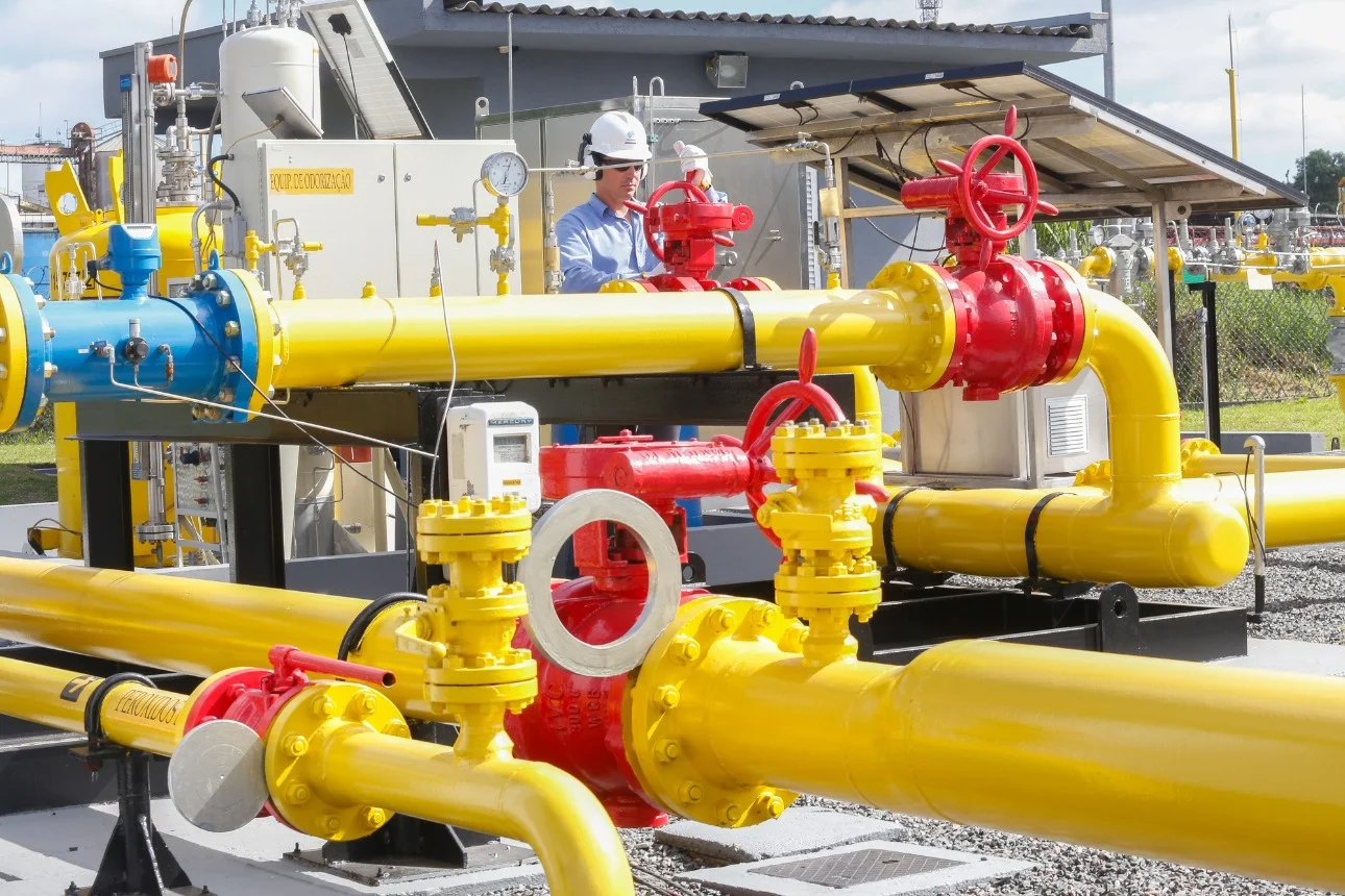 Citygate (ponto de entrega de gás) da Compagas, distribuidora de gás natural do Paraná; Rede de gasodutos nas cores amarela e vermelha, com trabalhador realizando inspeção; veste uniforme azul e capacete branco (Foto: Divulgação)