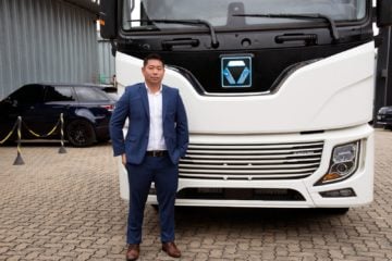 Fabricante chinesa XCMG mira eletrificação de máquinas e veículos pesados no Brasil. Na imagem: Ricardo Hidemi Senda, head de veículos elétricos da XCMG, em frente a caminhão branco da fabricante chinesa (Foto: Divulgação)