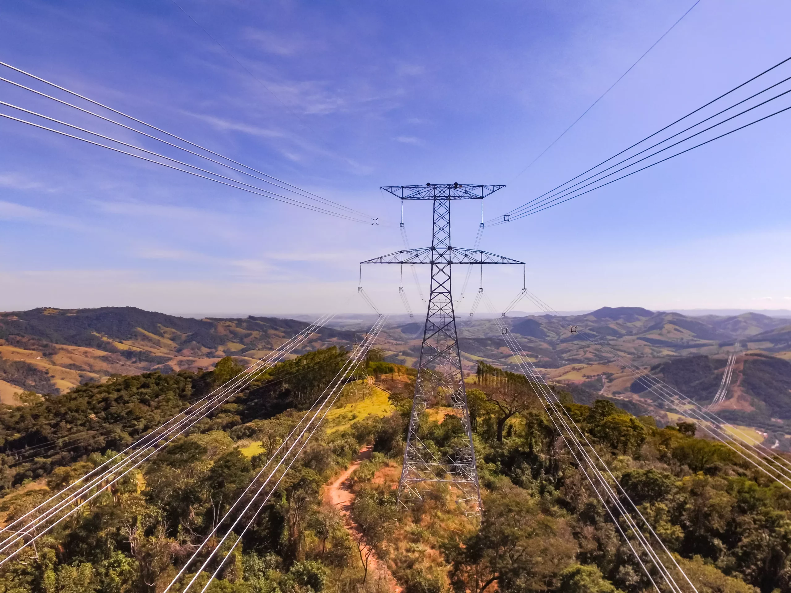 Entenda que está em jogo na criação do mercado livre de energia elétrica e principais impactos para o setor. Na imagem: Sistema de transmissão de energia Cantareira, entre MG e SP, da Elecnor do Brasil. Linhas de transmissão, em primeiro plano, e torre de grande porte, ao fundo, com céu azul (Foto: Divulgação)