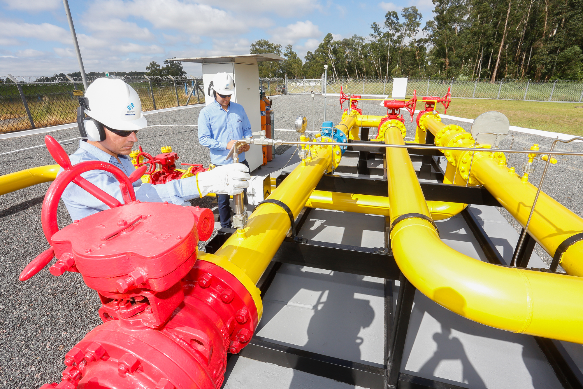 Conselho da Copel avança nos preparativos para venda da Compagas, distribuidora paranaense. Na imagem: Citygate (ponto de entrega de gás) da Compagas, distribuidora de gás natural do Paraná; Rede de gasodutos nas cores amarela e vermelha, com dois trabalhadores realizando inspeção; vestem uniforme azul, capacete branco e óculos escuros, equipamentos de proteção individual (Foto: Divulgação)