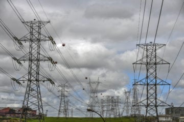 Torres de transmissão de energia com cabos de alta tensão sob céu encoberto de nuvens acinzentadas