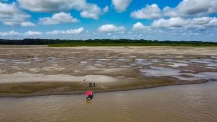 Os oportunistas nossos de cada dia e a falta de um debate técnico no setor elétrico. Na imagem: Vista de grande banco de areia aparente devido a baixa vazão por conta da seca no Rio Madeira, na Bacia Amazônica; com pequena embarcação junto à margem e, ao lado, três pessoas conversam (Foto: Defesa Civil/AM)