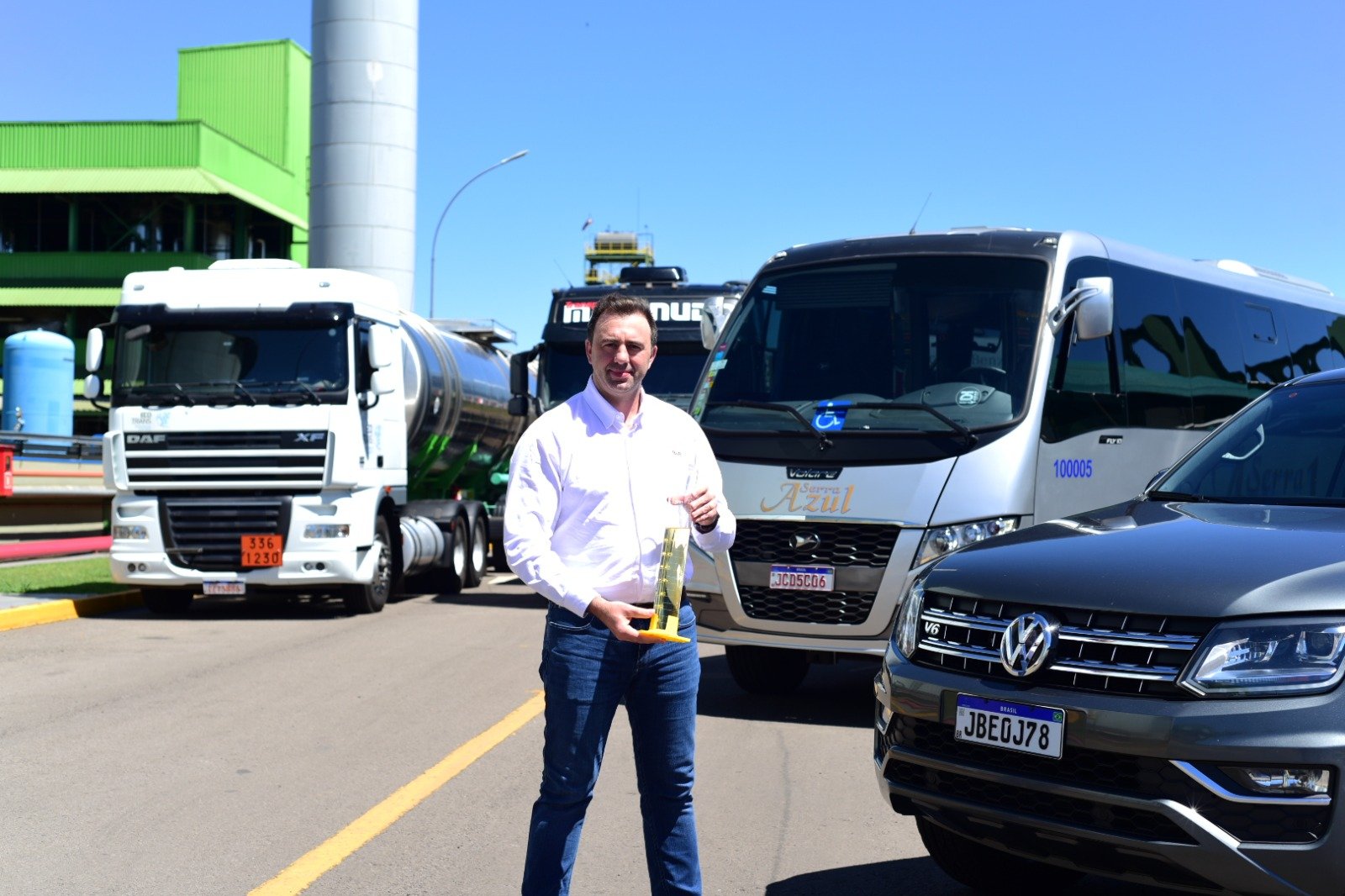 Be8 (ex-BSBIOS) lança novo biocombustível drop-in para substituir diesel fóssil em até 100% . Na imagem: Erasmo Carlos Battistella, presidente da Be8, segura longo frasco laboratorial de vidro contendo combustível líquido de cor amarelada; ao fundo, lado a lado, um caminhão, um ônibus, um micro ônibus e um carro (Foto: Divulgação)