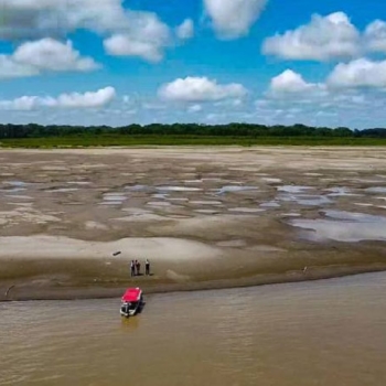 Ação lenta no financiamento dobra o custo de adaptação às mudanças climáticas. Na imagem: Vista de grande banco de areia aparente devido a baixa vazão por conta da seca no Rio Madeira, na Bacia Amazônica; com pequena embarcação junto à margem e, ao lado, três pessoas conversam (Foto: Defesa Civil/AM)