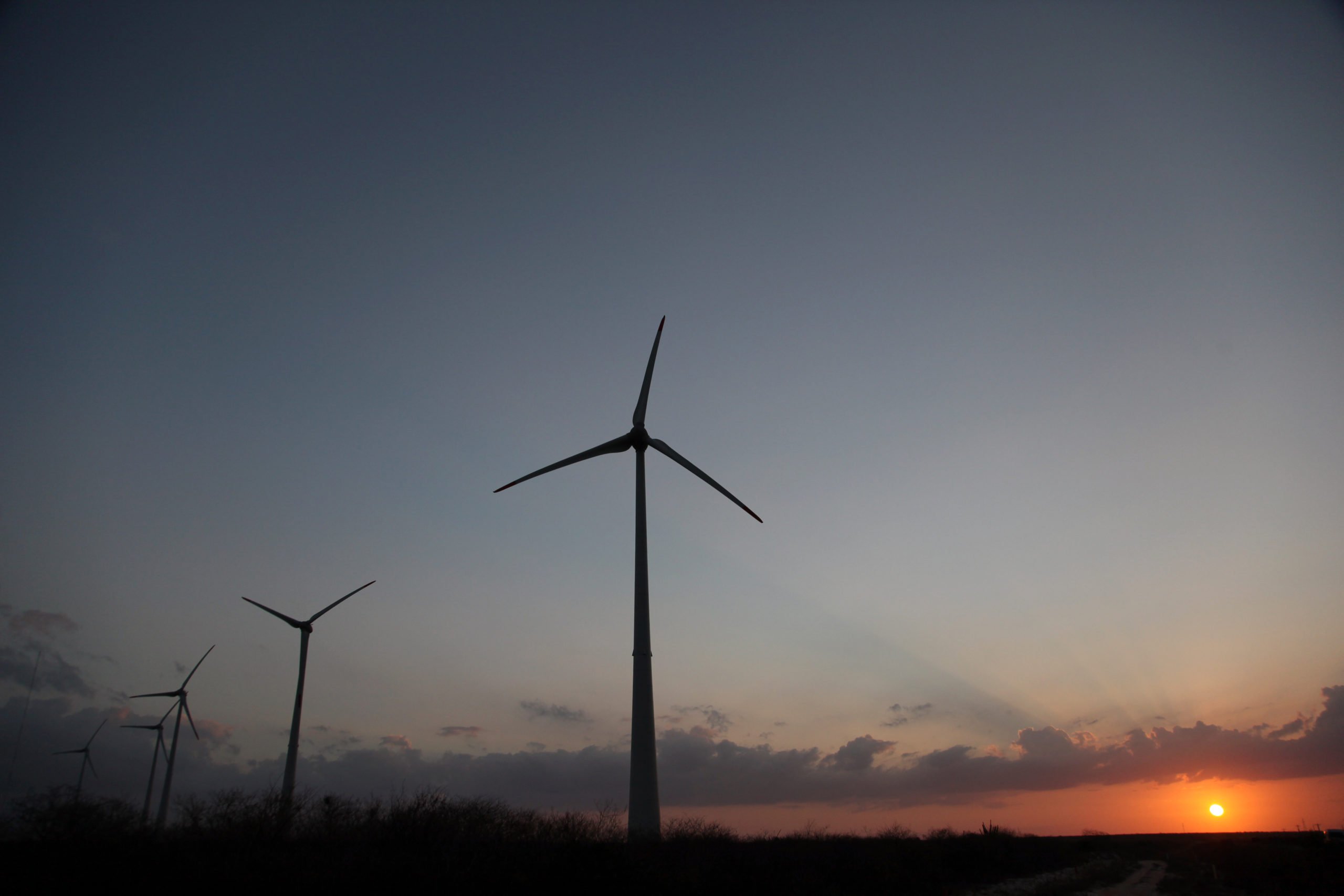 Petrobras investirá US$ 5,2 bilhões em energia  eólica e solar até 2028, mostra novo plano de negócios. Na imagem: Turbinas eólicas fotografadas ao anoitecer, à contraluz, com sol se pondo ao fundo (Foto: Divulgação Petrobras)