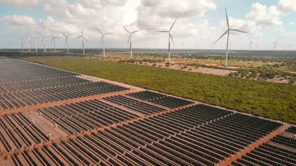 Brasil instala 7GW de eólica e solar até outubro de 2023. Na imagem: Vista de usina híbrida eólica e solar fotovoltaica, com inúmeras fileiras de módulos fotovoltaicos, em primeiro plano, e aerogeradores, ao fundo, à direita (Foto: Divulgação Voltalia)