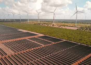 Brasil instala 7GW de eólica e solar até outubro de 2023. Na imagem: Vista de usina híbrida eólica e solar fotovoltaica, com inúmeras fileiras de módulos fotovoltaicos, em primeiro plano, e aerogeradores, ao fundo, à direita (Foto: Divulgação Voltalia)