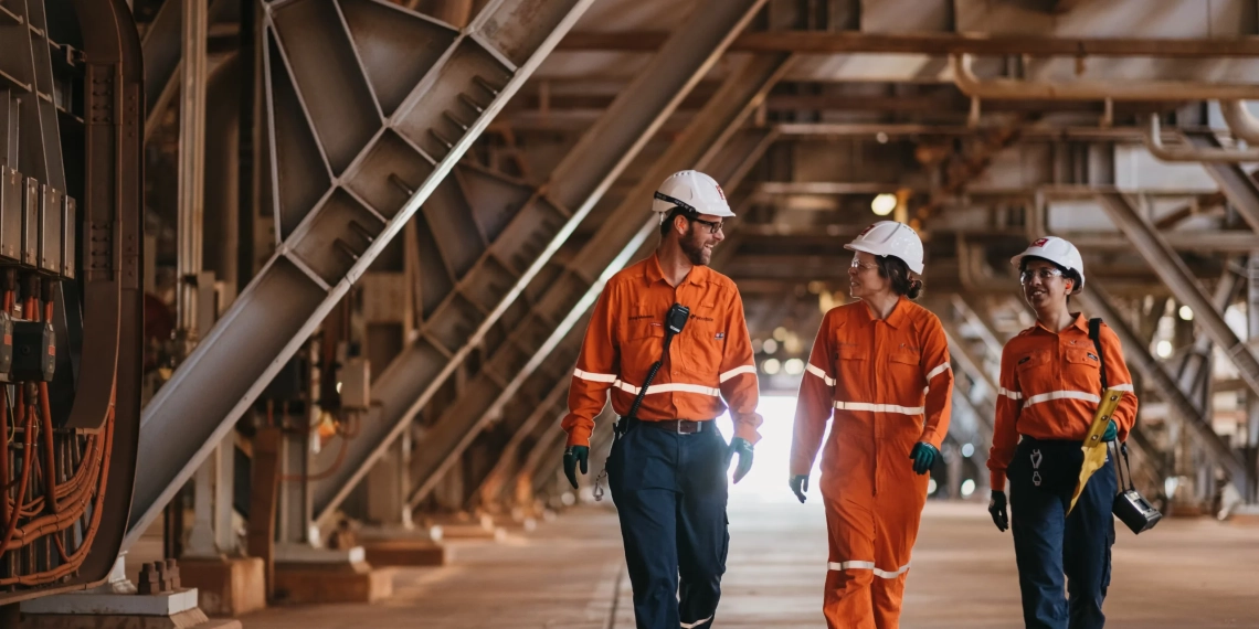 Australianas Woodside Energy e Santos negociam fusão para criar gigante do gás natural. Na imagem: Três trabalhadores (um homem e duas mulheres) conversam enquanto caminham na planta de GNL Pluto, da Woodside, que processa gás natural dos campos offshore de Plutão e Xena, na Austrália Ocidental (Foto: Jarrad Seng)