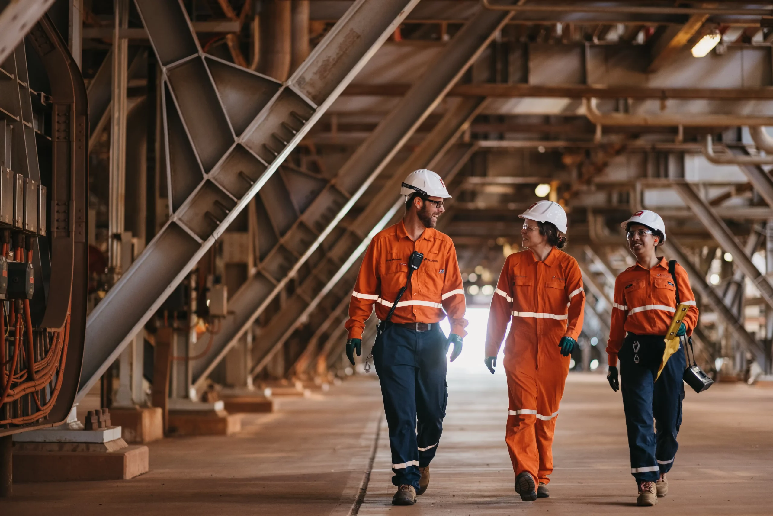 Australianas Woodside Energy e Santos negociam fusão para criar gigante do gás natural. Na imagem: Três trabalhadores (um homem e duas mulheres) conversam enquanto caminham na planta de GNL Pluto, da Woodside, que processa gás natural dos campos offshore de Plutão e Xena, na Austrália Ocidental (Foto: Jarrad Seng)