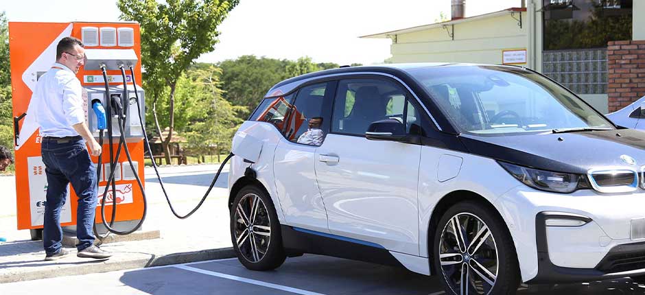 Brasil deve contar com quase 7 mil eletropostos operando até final de 2024 para recarga de elétricos. Na imagem: Homem opera aplicativo em celular que auxilia na recarga de veículo elétrico SUV na cor branca (Foto: Reprodução Agência de Notícias do Paraná)