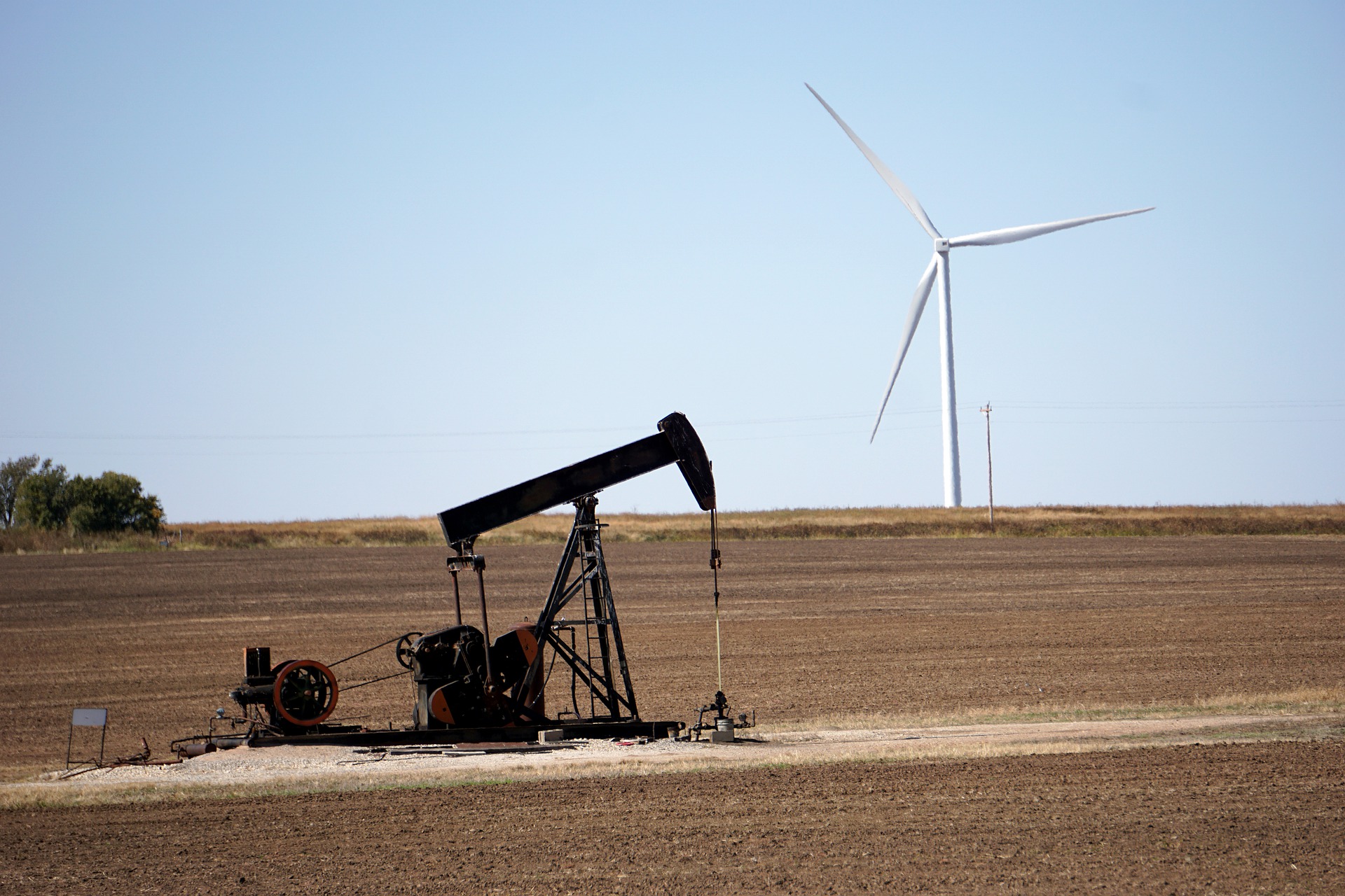 Emissões globais de energia aumentam, mesmo com recordes de geração de energias renováveis. Na imagem: Bomba de petróleo para exploração onshore em um terreno descampado, com turbinas eólicas ao fundo (Foto: Michael/Pixabay)