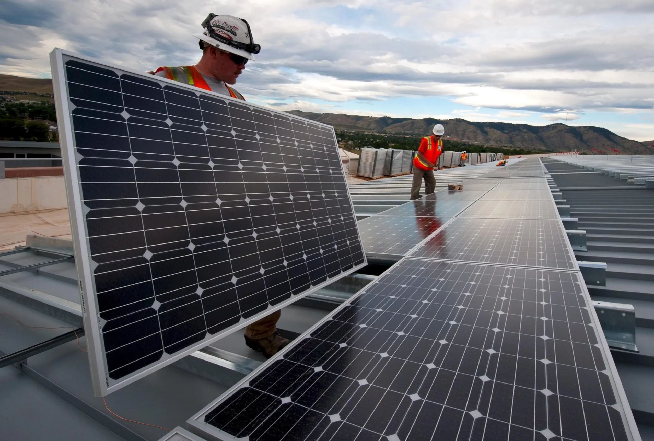 Custo médio para instalar painéis solares fotovoltaicos no Brasil cai no 1º trimestre com menor preço de matéria-prima. Na imagem: Trabalhadores instalam painéis fotovoltaicos sobre uma longa extensão; vestem colete de proteção laranja e capacetes brancos com lanternas acopladas (Foto: Skeeze/Pixabay)