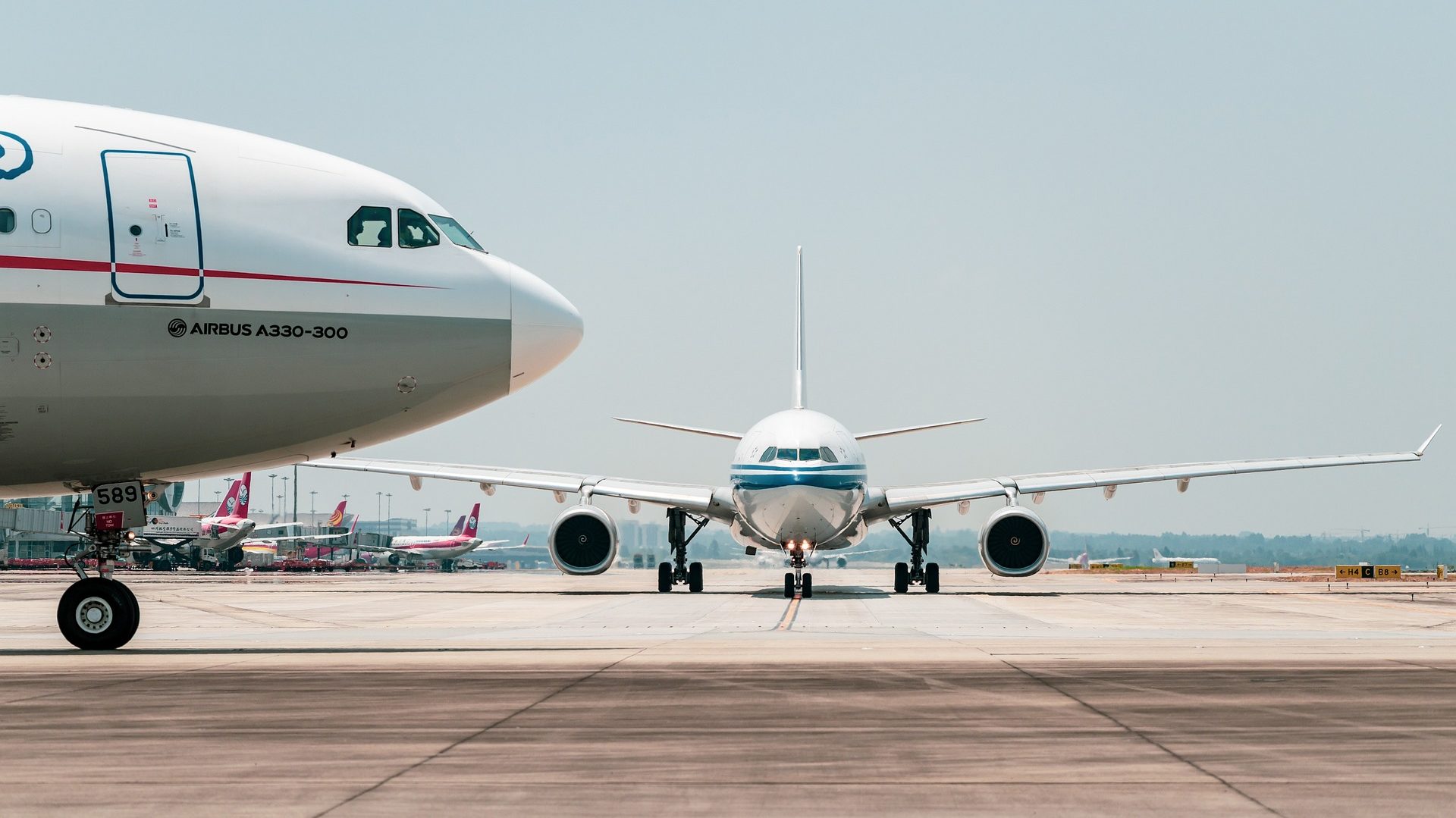 Brasil enfrenta desafio de descarbonizar aviação sem perder passageiros e Ministério de Portos defende mais discussões sobre tributação de combustível sustentável (SAF). Na imagem: Visão lateral da parte frontal de aeronave e, ao fundo, visão frontal de outro avião, em pista de aeroporto (Foto: 穿着拖鞋一路小跑/Pixabay)