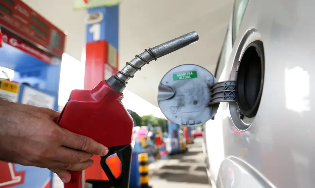 Mão de frentista segura bomba de abastecimento vermelha em posto de combustíveis próximo a abertura do tanque do automóvel (Foto: Marcelo Camargo/Agência Brasil)