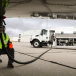 Trabalhador conecta mangueira de caminhão tanque à compartimento na parte de baixo da asa de aeronave para abastecimento (Foto Divulgação EiDA)
