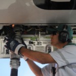 Homem branco conecta, &agrave; parte de baixo de aeronave, mangueira para abastecimento de aeronave com SAF, biocombust&iacute;vel de avia&ccedil;&atilde;o (Foto: T&acirc;nia R&ecirc;go/Ag&ecirc;ncia Brasil)