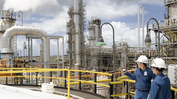 Disputa pela Braskem: por que petroquímica atrai investidores ao redor do mundo. Na imagem: Trabalhadores uniformizados e com equipamentos de proteção em refinaria da Braskem, com instalações metálicas e chaminés ao fundo (Foto: João Musa/Divulgação)