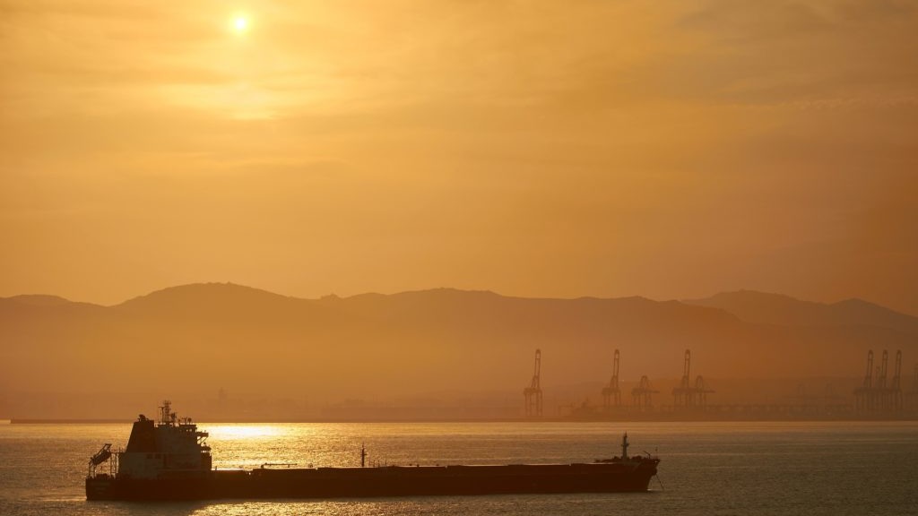 Mercado de petróleo volta atenções para política monetária de juros no Brasil e nos Estados Unidos. Na imagem: Navio tanque transporta petróleo com céu em tons de amarelo com pôr do sol, e montanha, ao fundo (Foto Creative Commons)