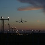 Anac publica detalhamento de regras para monitoramento e compensação de emissões de GEE em voos internacionais. Na imagem: Avião voando ao anoitecer com uma série de postes sinalizadores, à esquerda (Foto Pixabay)