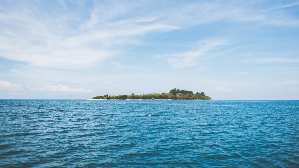 Na imagem: Vista de ondulações do mar azul e, ao fundo, ilha coberta com vegetação (Foto Pexels/Pixabay)