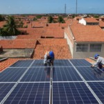 Dois trabalhadores instalam placas fotovoltaicas sobre telhado para geração solar (Foto Natinho Rodrigues)