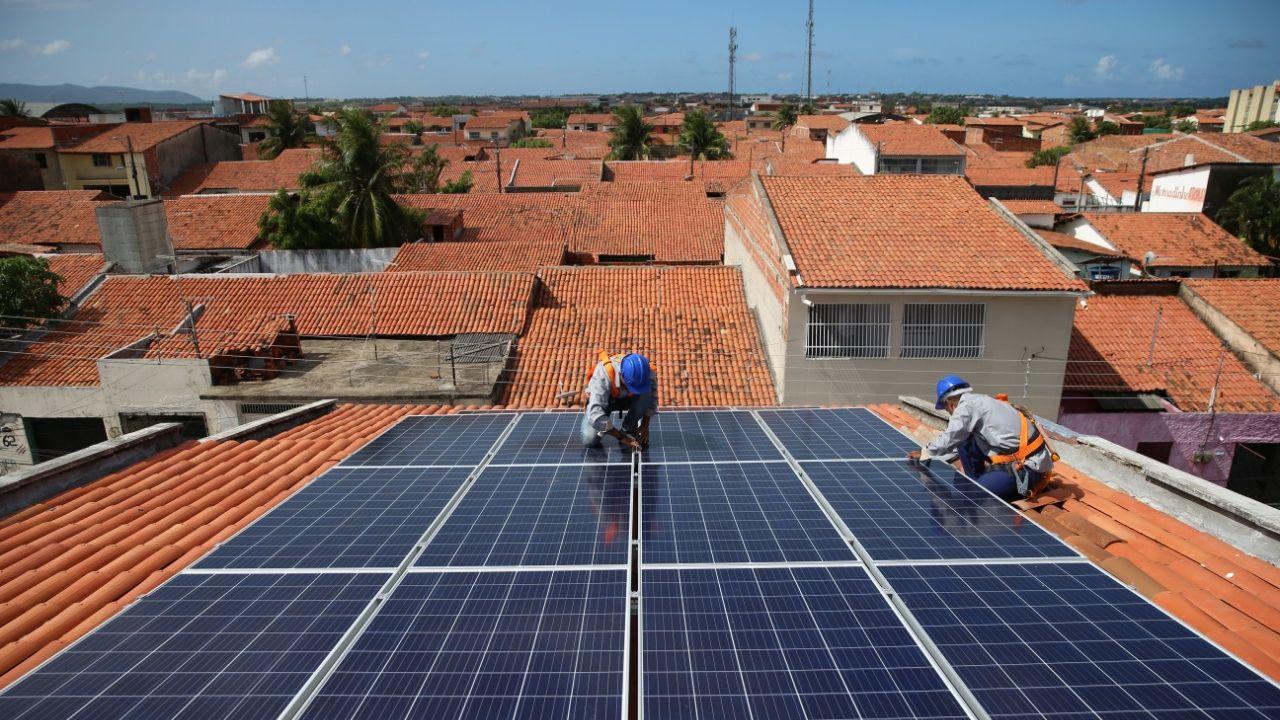 Dois trabalhadores instalam placas fotovoltaicas sobre telhado para geração solar (Foto Natinho Rodrigues)